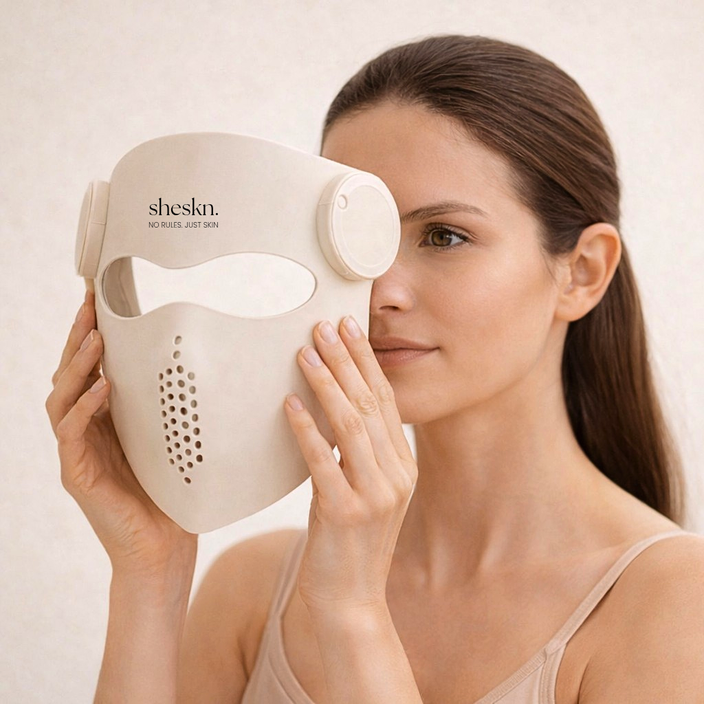 Model holding the Sheskn Luméskn LED face mask near her face before applying, showing the flexible silicone design and centred forehead logo.