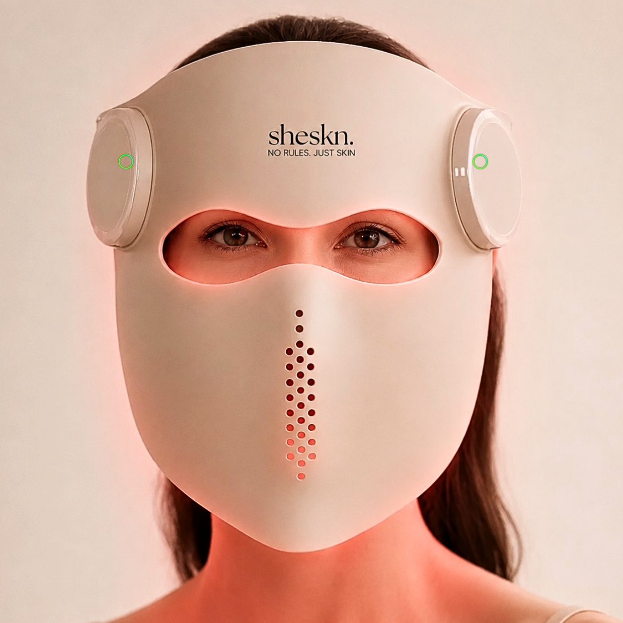 SHESKN Luméskn LED Face Mask using red light therapy with a soft red glow illuminating the face and neck.